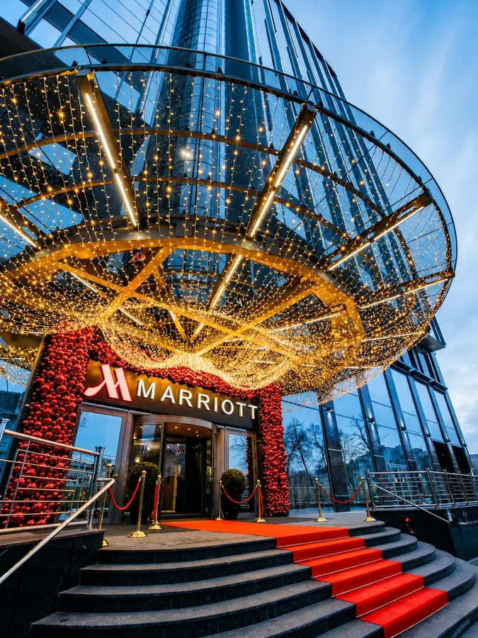 Парадный вход Marriott с подсвеченным стеклянным навесом, красной дорожкой и декоративным оформлением.