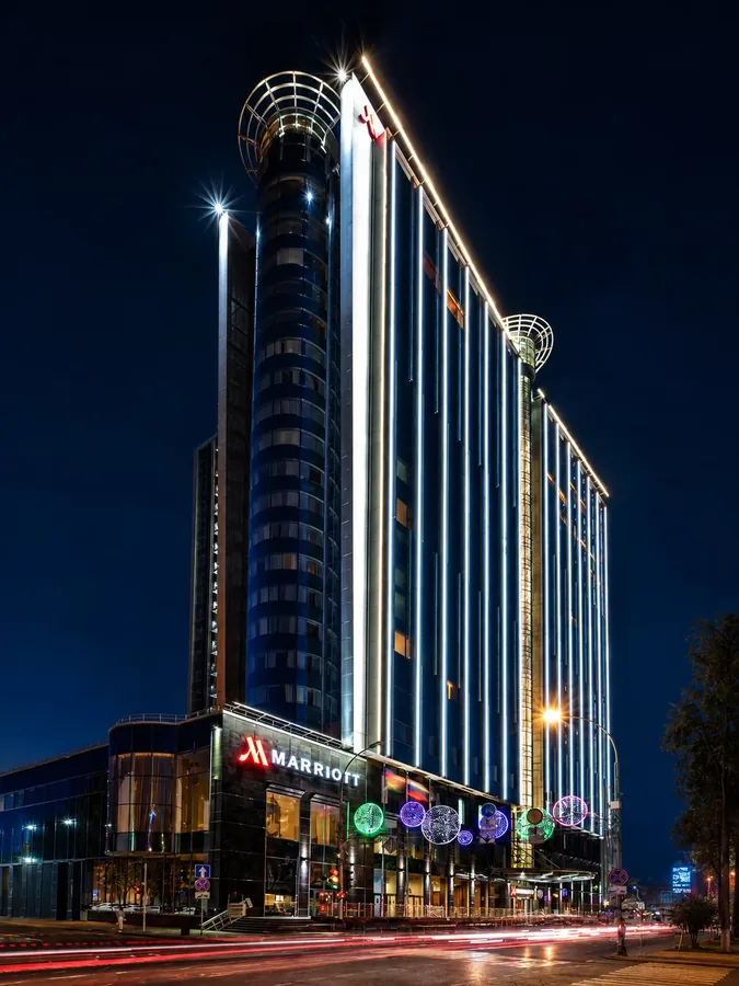 Ночной фасад высотного отеля Marriott с вертикальной подсветкой и световыми следами транспорта.