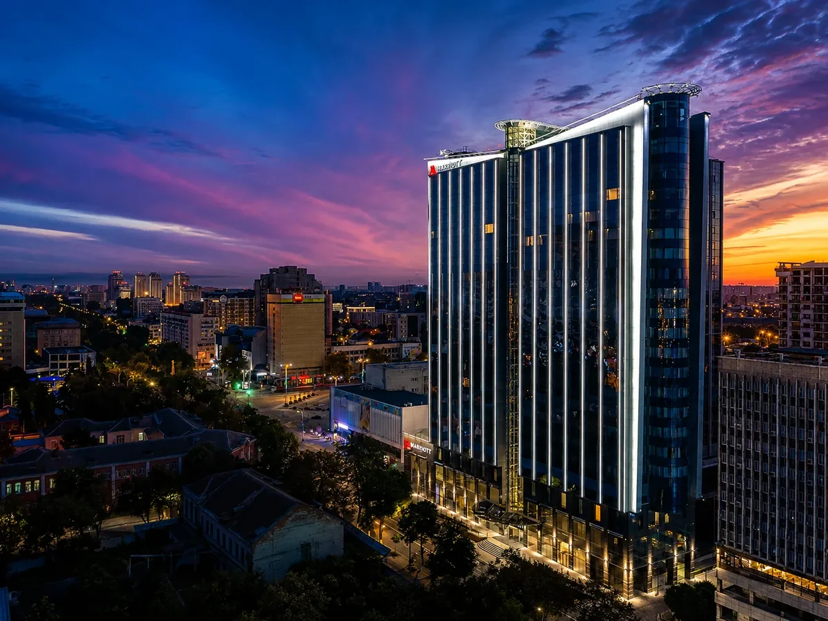 Высотный отель Marriott в городском пейзаже на закате с яркой фасадной подсветкой.